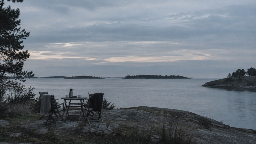 Two empty chairs and a shared table overlooking still water, representing why self-reflection alone doesn't work.